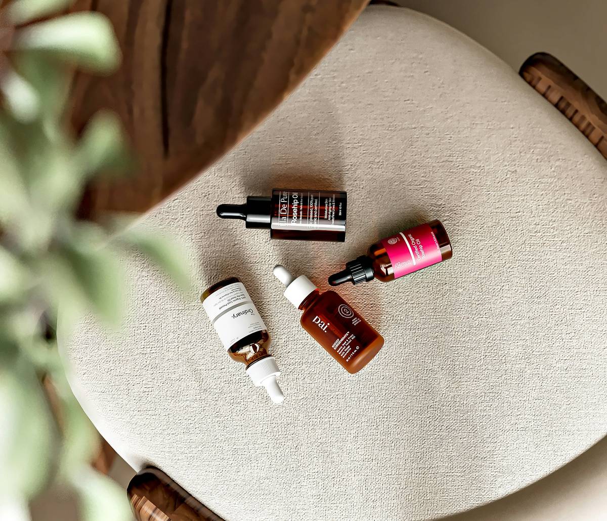 Glass dropper bottle of golden plant-infused beauty oils against a backdrop of fresh organic herbs like rosemary and lavender